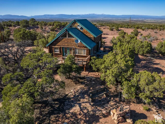 Log cabin exterior with a teal metal roof, multi-level decking, and a stone fire pit area