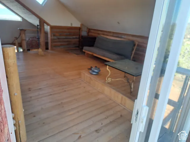 Sloped ceiling with skylights, wood-finish flooring, log-style wall paneling, and a sliding glass door