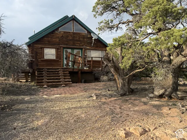 Log cabin exterior featuring a green roof, triangular transom windows, a wood deck with log railing, and log steps over a paver stone landing