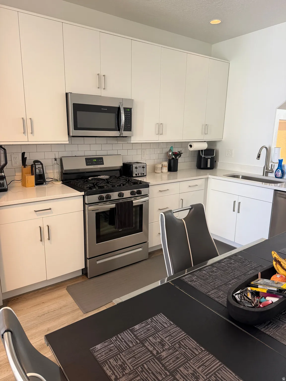 Modern kitchen featuring white flat-panel cabinetry, stainless steel appliances, a subway tile backsplash, and light wood-finish flooring