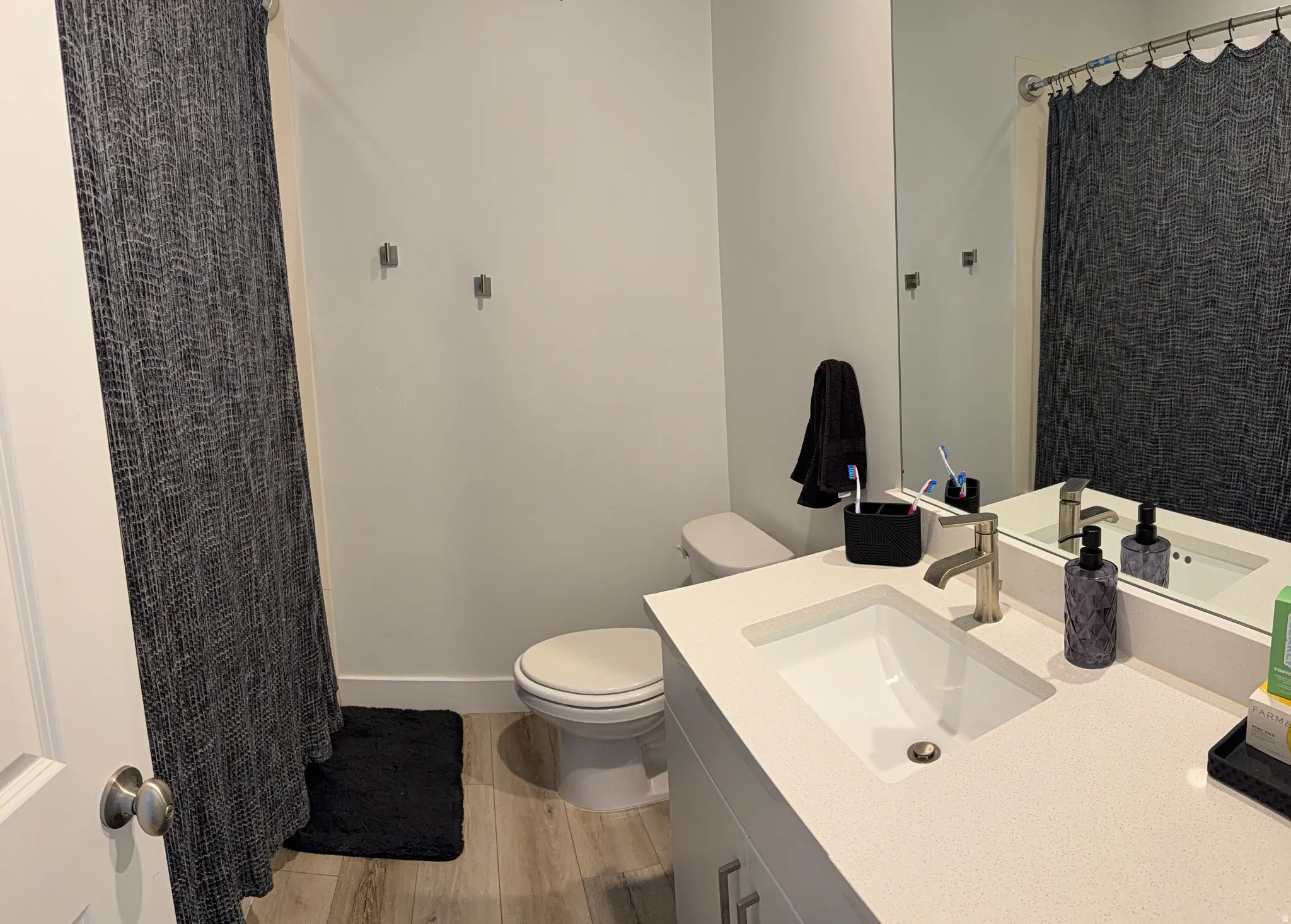 Bathroom featuring a single vanity with an integrated sink, brushed nickel faucet, large wall mirror, and wood-finish flooring