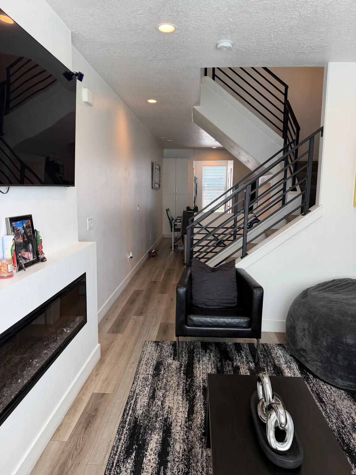 Integrated linear fireplace with a white mantel, wood-finish flooring, and modern open-riser staircase with horizontal metal railings