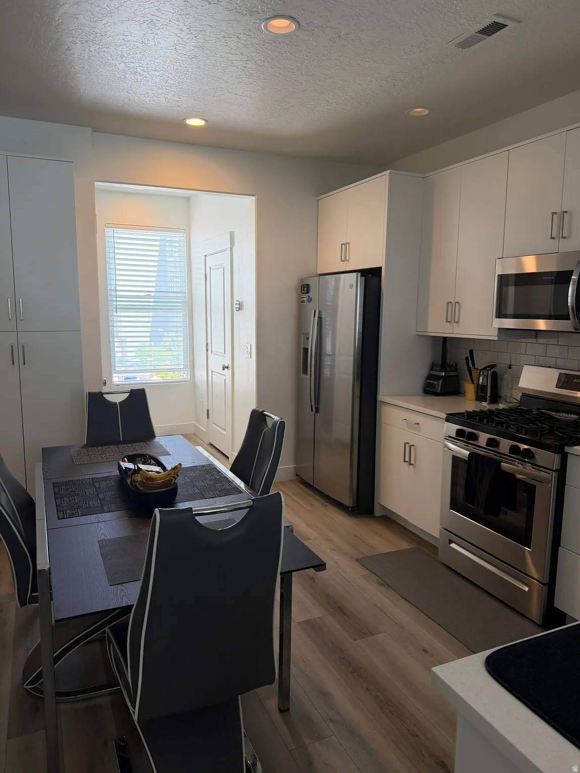 Modern kitchen featuring white cabinetry, stainless steel appliances, light countertops, and a white subway tile backsplash