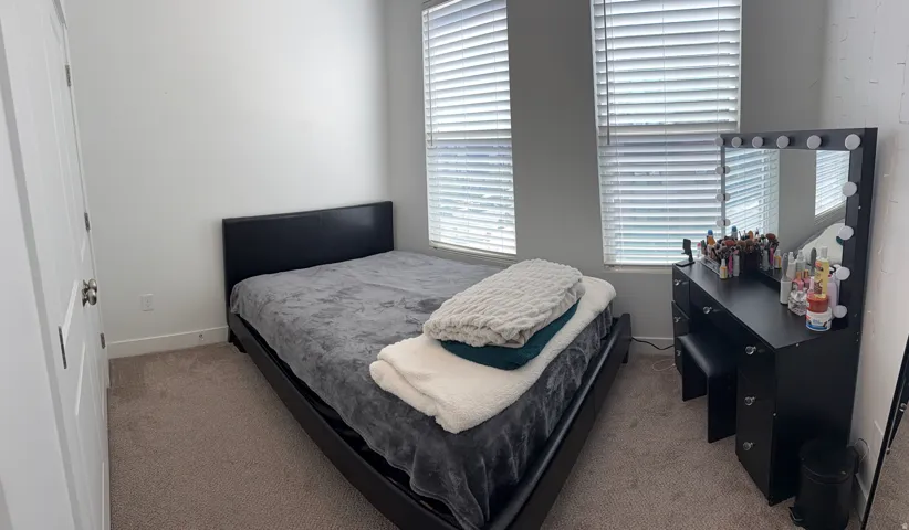 Bedroom featuring two windows with horizontal blinds, light gray walls, and carpet flooring
