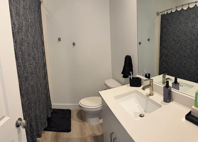 Bathroom featuring a single vanity with an integrated sink, brushed nickel faucet, large wall mirror, and wood-finish flooring