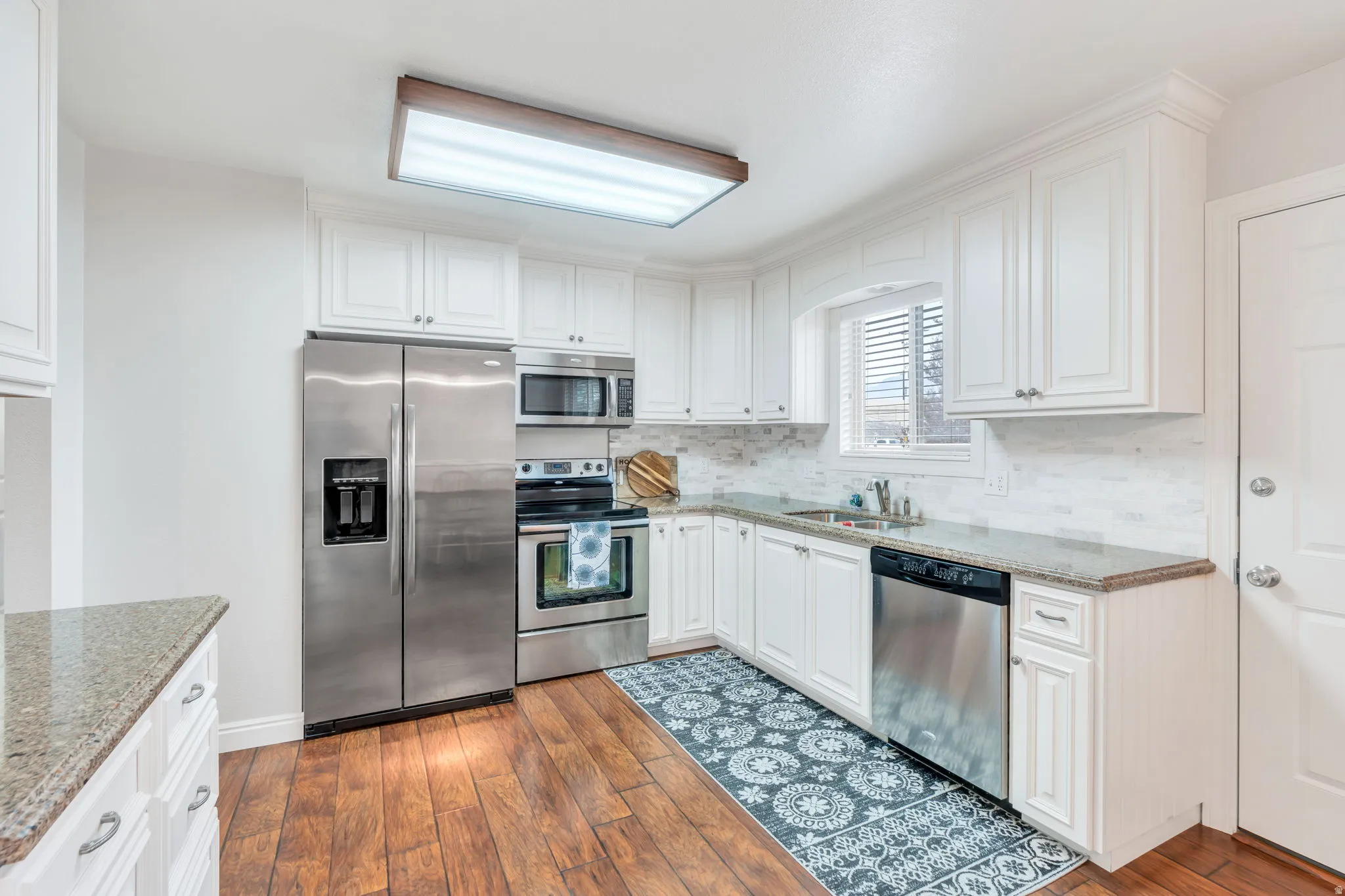 Kitchen featuring white cabinetry, granite countertops, stainless steel appliances, wood-finish flooring, and a tiled backsplash