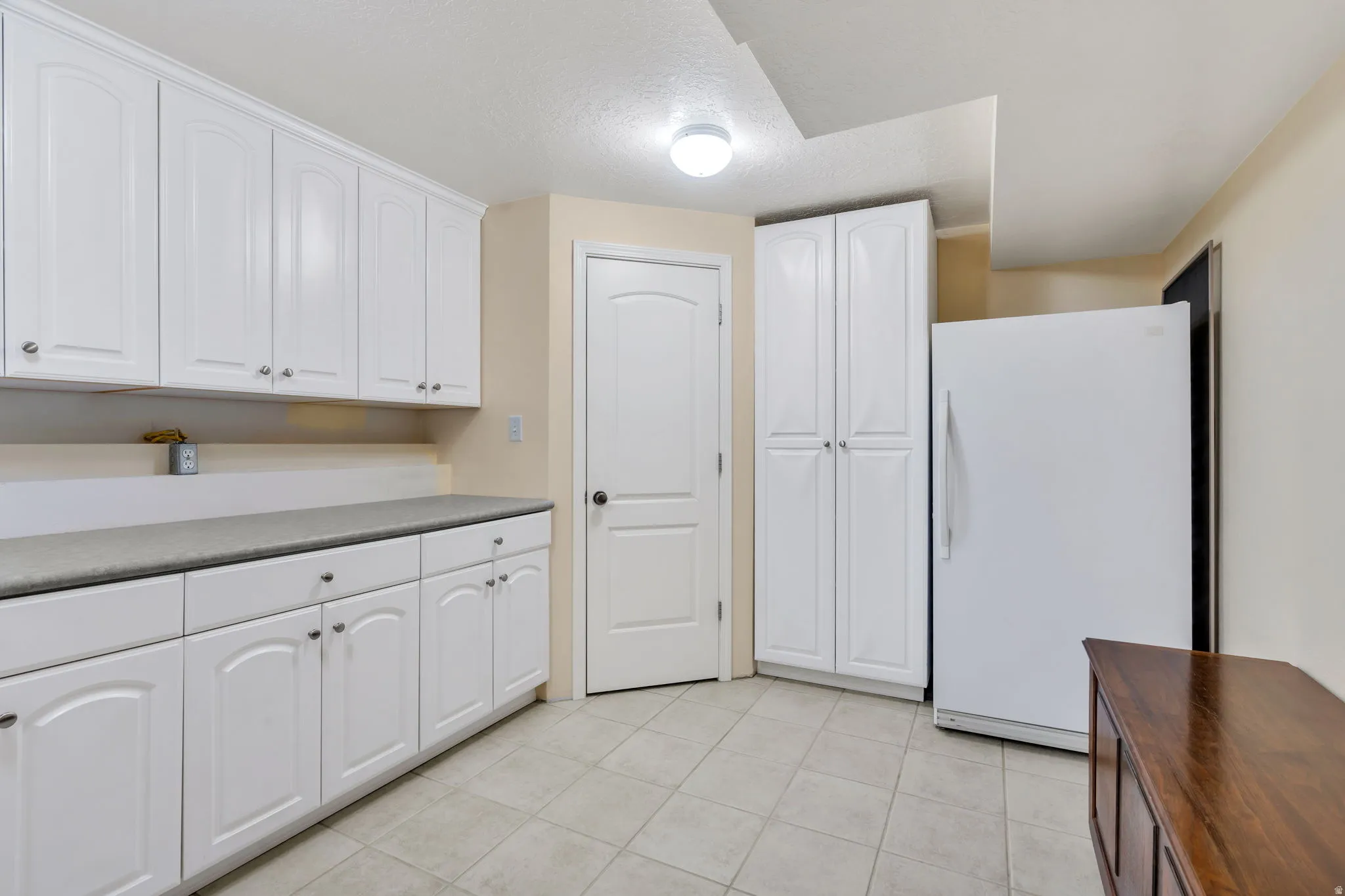 Kitchen area featuring extensive white cabinetry, a light-colored countertop, and square tile flooring