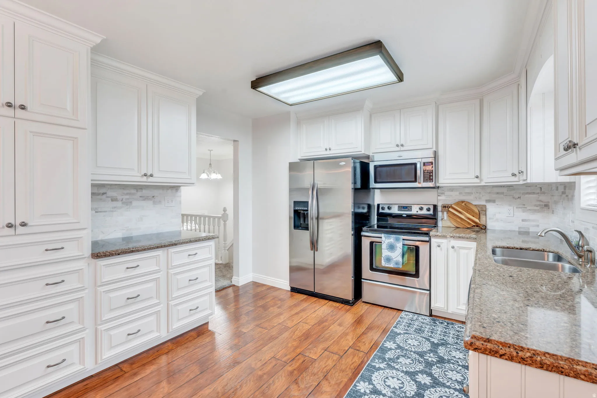 Kitchen featuring extensive white cabinetry, wood-finish flooring, stone countertops, stainless steel appliances, and a tiled backsplash