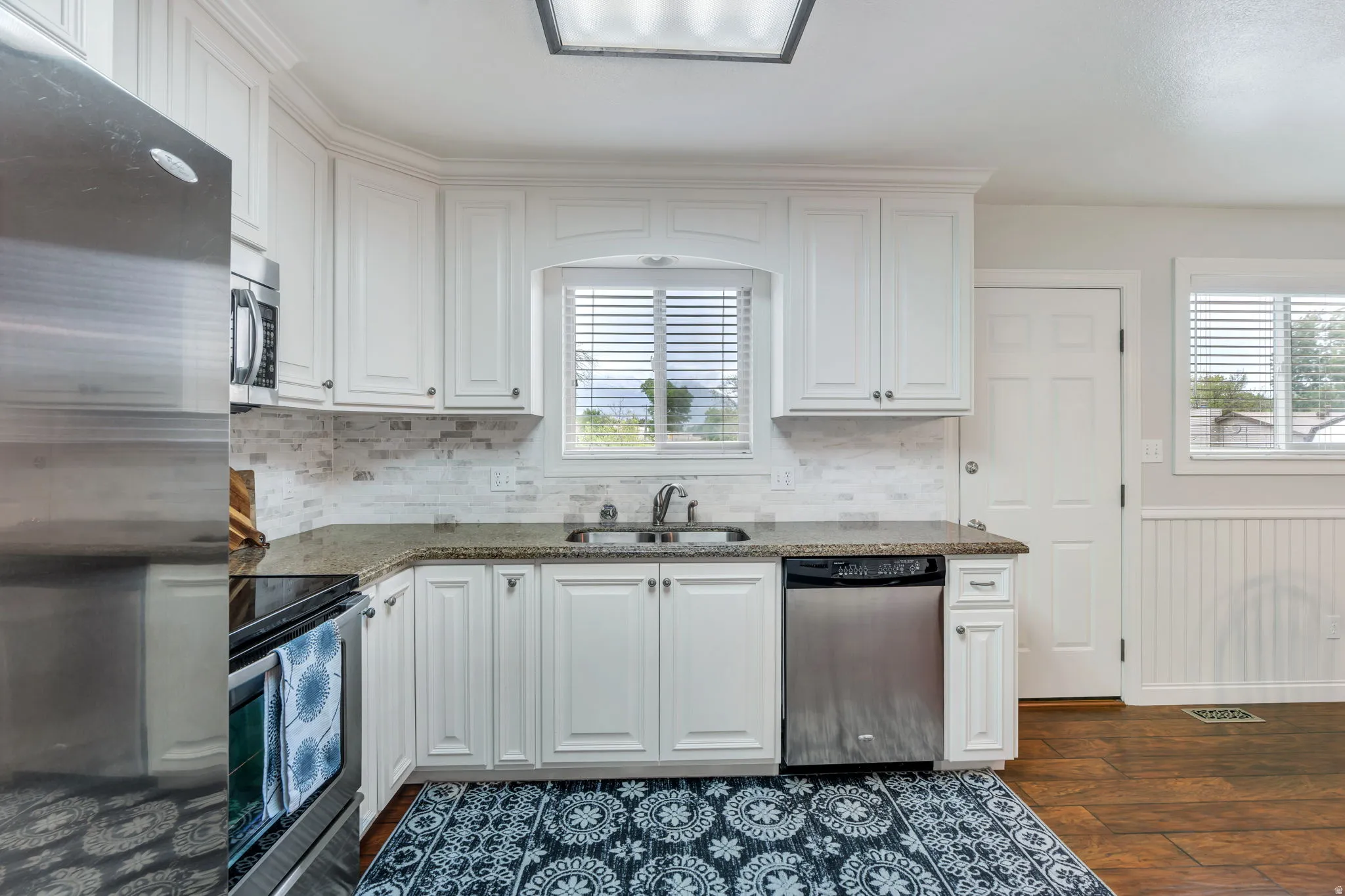 Kitchen featuring white cabinetry, stainless steel appliances, speckled countertops, a tile backsplash, and wood-finish flooring