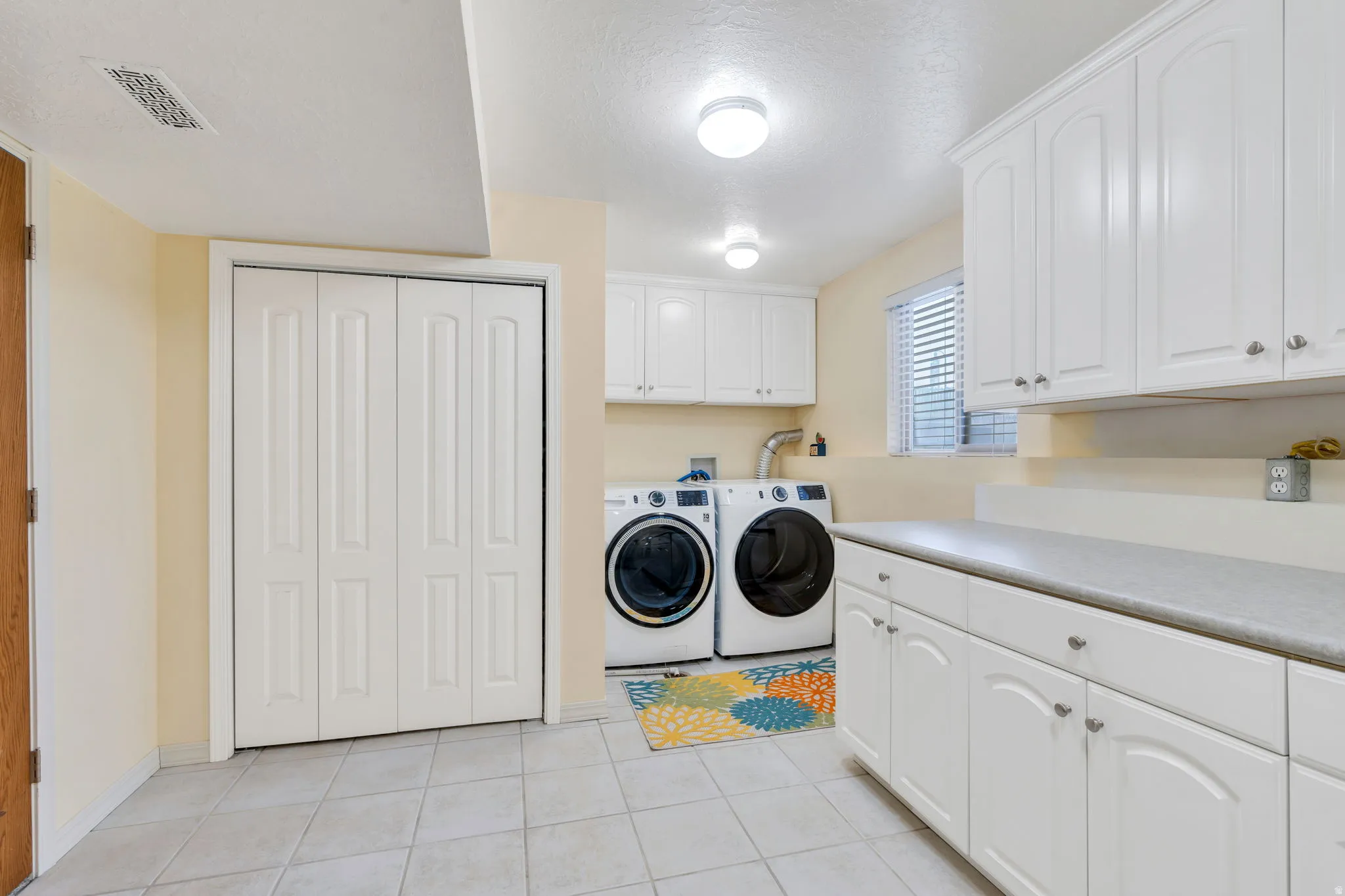 Laundry area featuring extensive white cabinetry, a light-colored countertop, and tile flooring