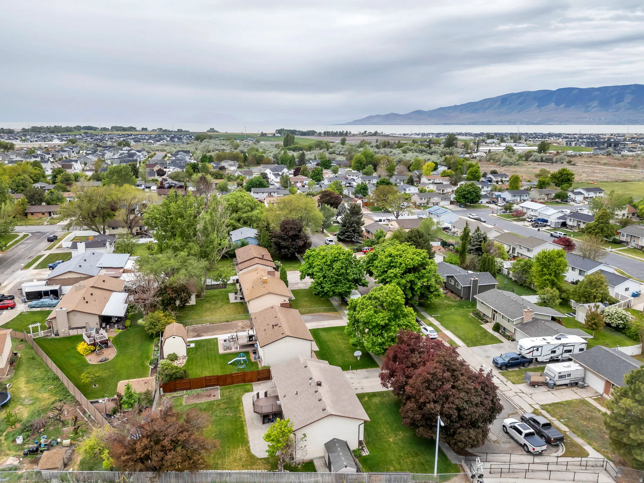 Aerial neighborhood overview featuring single-family residences with mature landscaping, a paved street grid, and a distant body of water with mountains