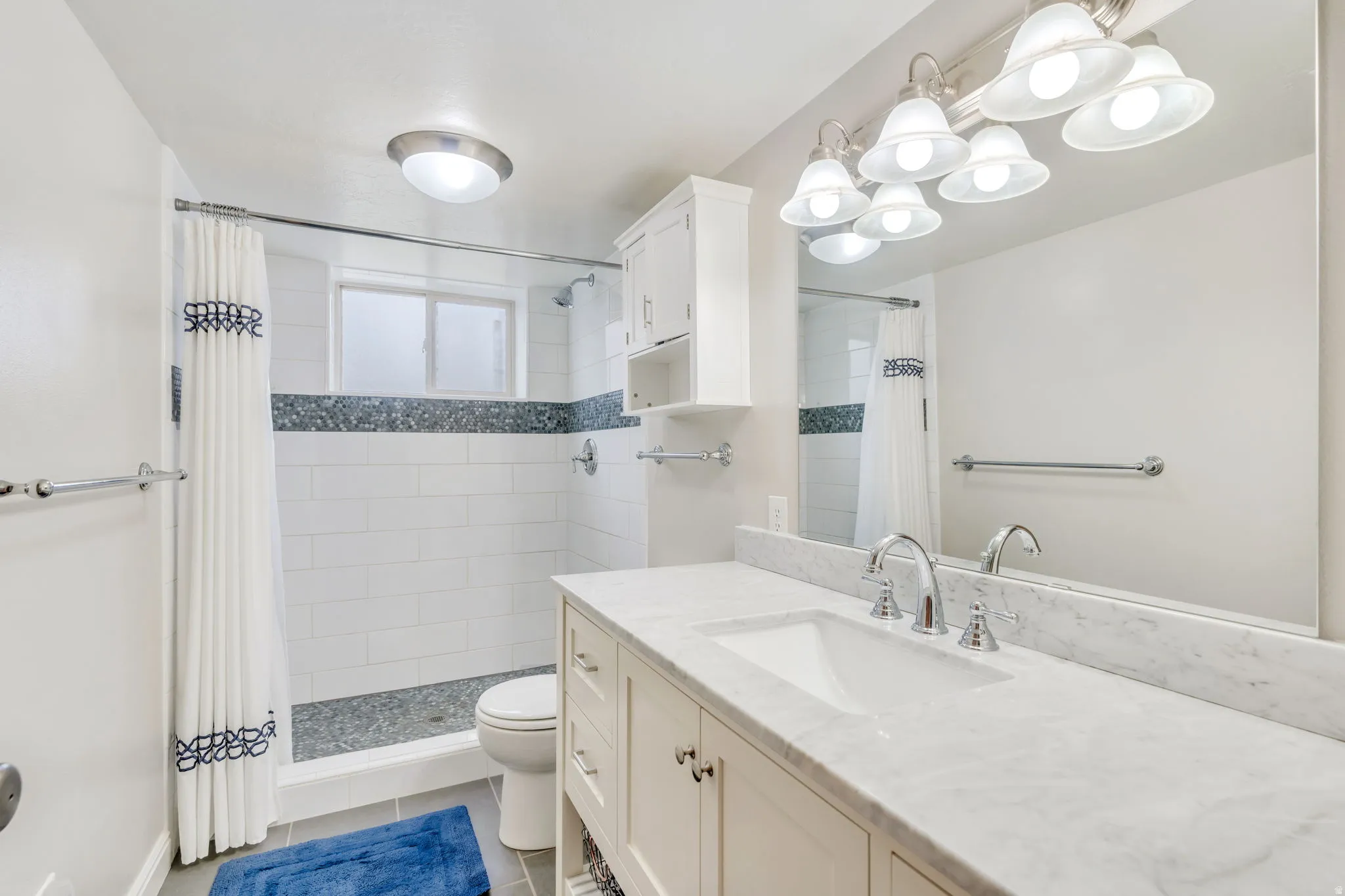 Bathroom featuring a single vanity with a white countertop and integrated sink, chrome-finish fixtures, and a large wall-mounted mirror