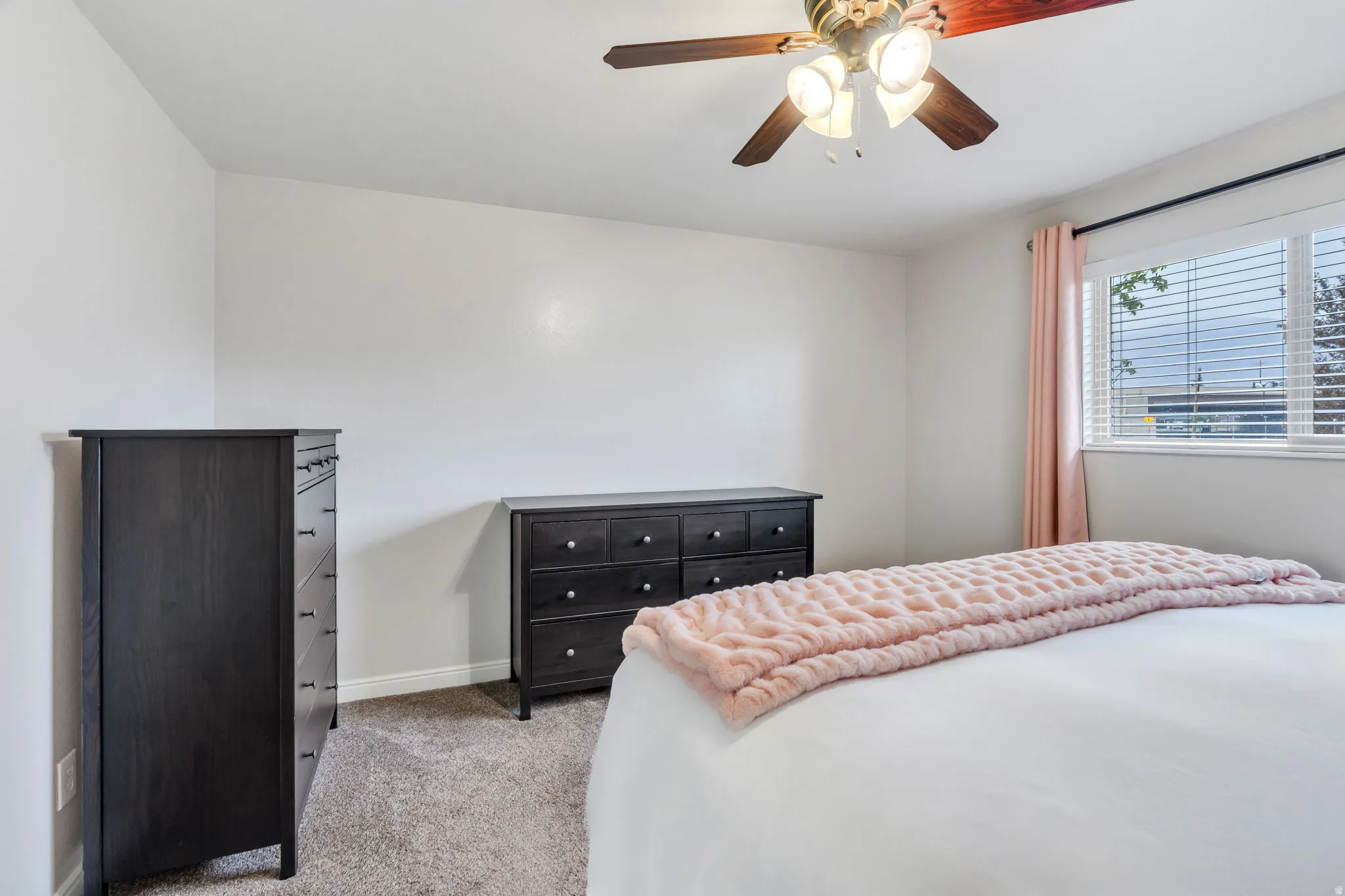 Carpeted bedroom with a ceiling fan light fixture, white walls, and a window with blinds