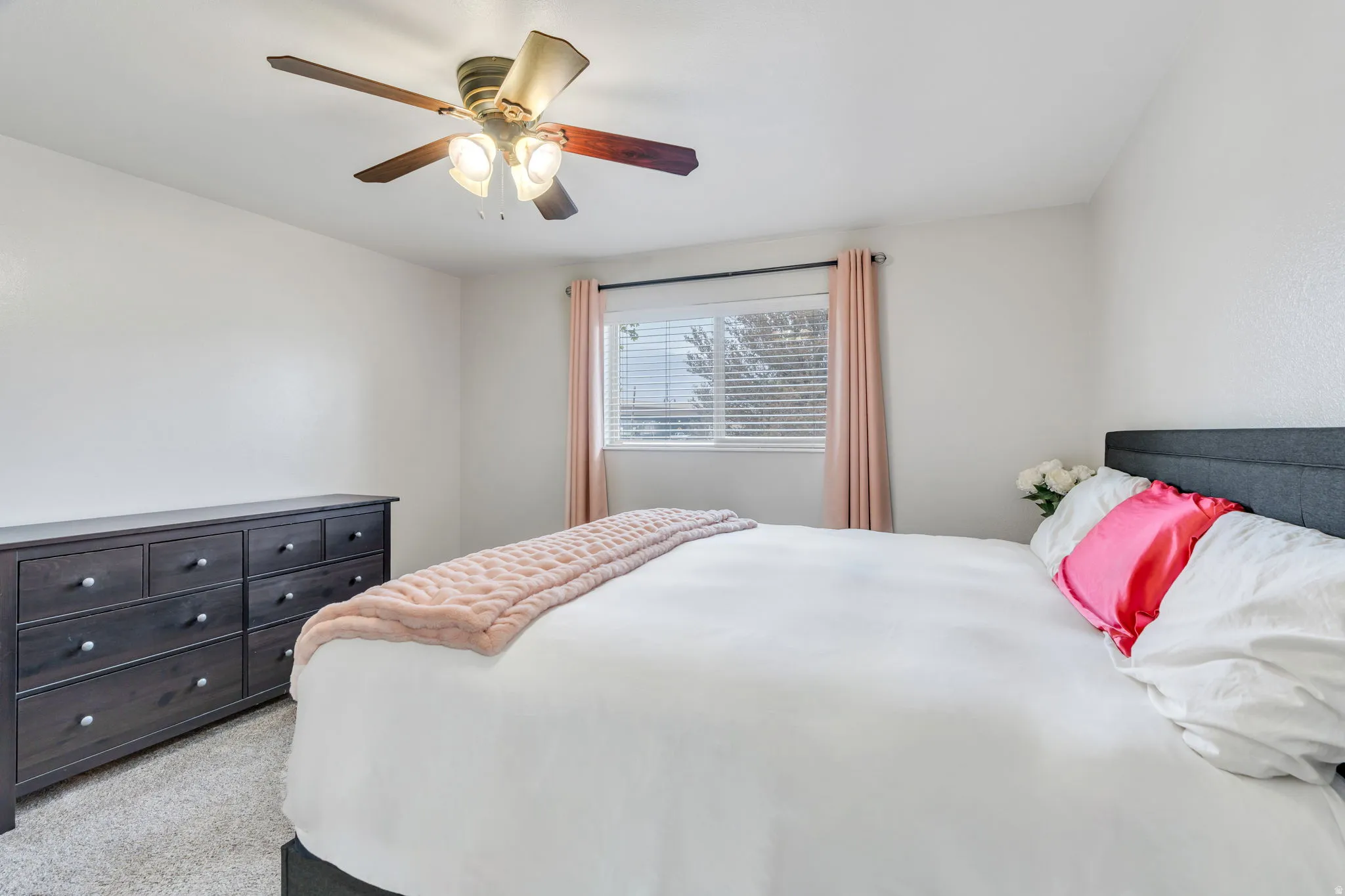 Carpeted bedroom featuring a ceiling fan with integrated lighting, a broad window with blinds and drapes, and a textured wall finish