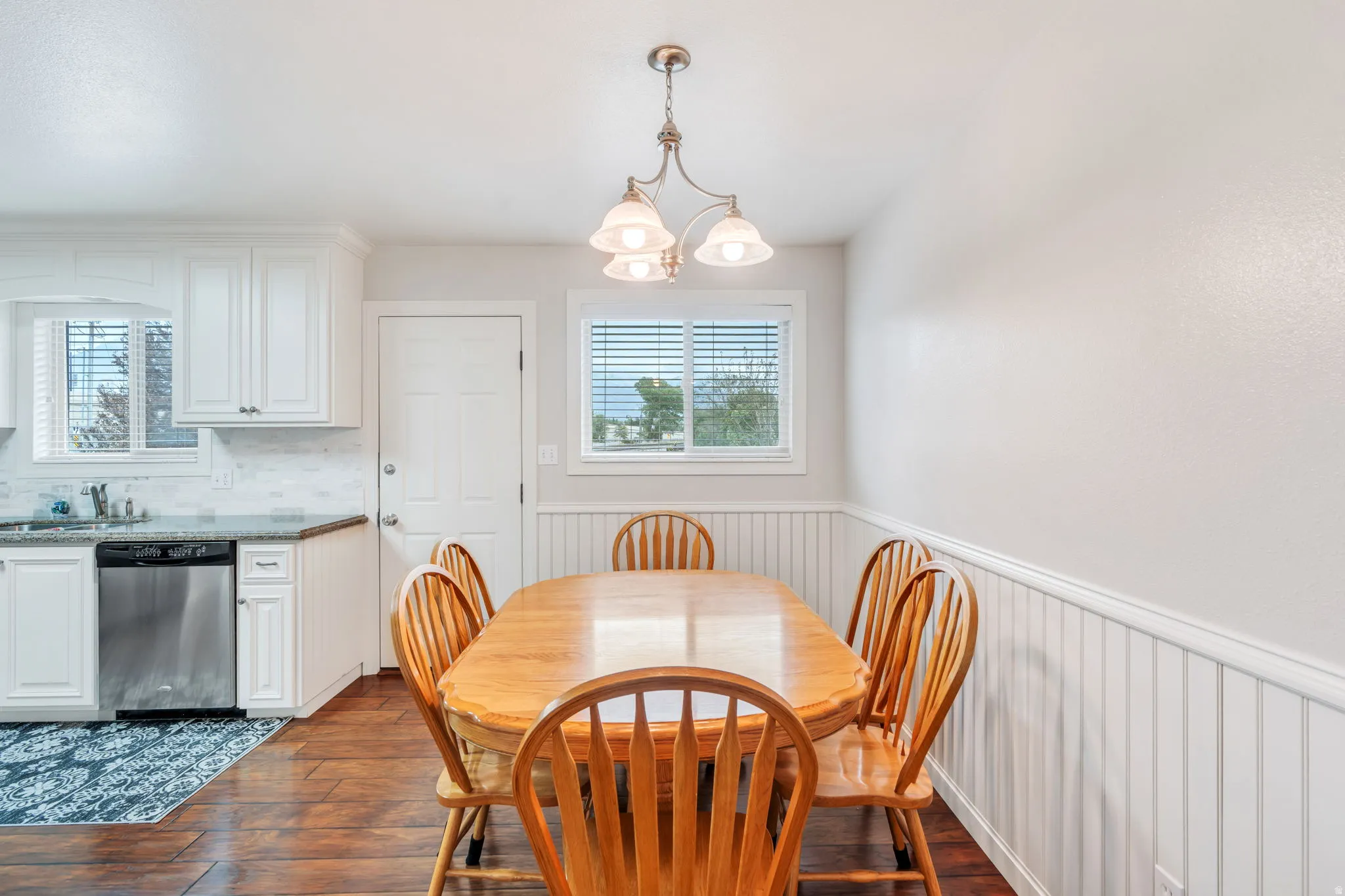 Dining area featuring wood-finish flooring, white wainscoting, and a multi-light pendant fixture