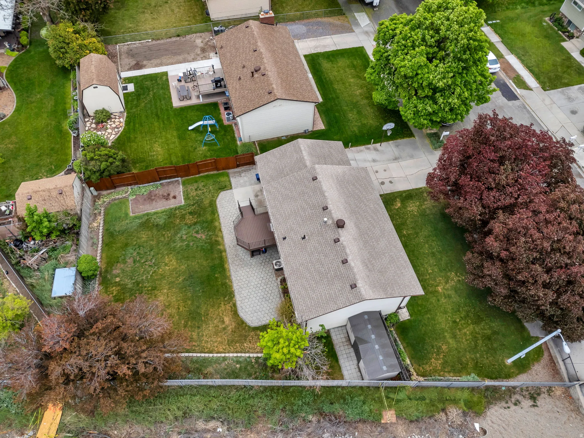 Expansive property featuring a two-story residence with a shingled roof, a spacious paved patio, and a tiered wood-decked outdoor area