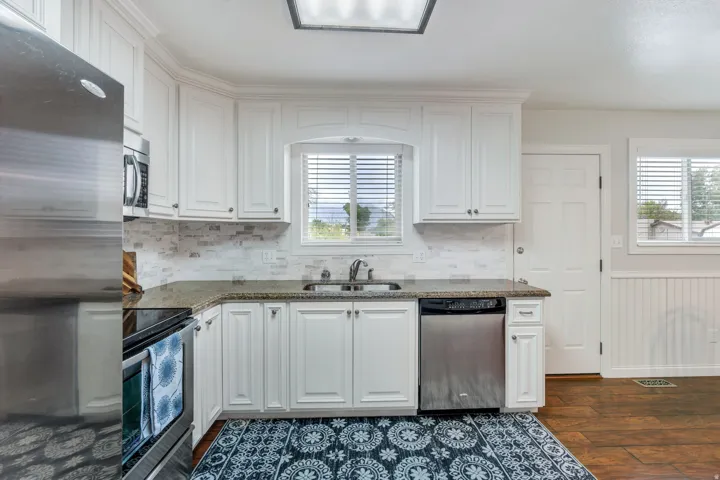 Kitchen featuring white cabinetry, stainless steel appliances, speckled countertops, a tile backsplash, and wood-finish flooring