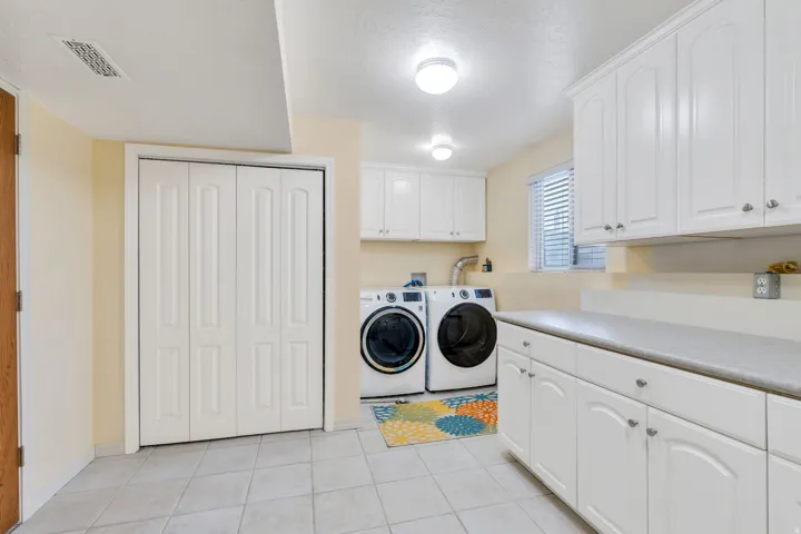Laundry area featuring extensive white cabinetry, a light-colored countertop, and tile flooring