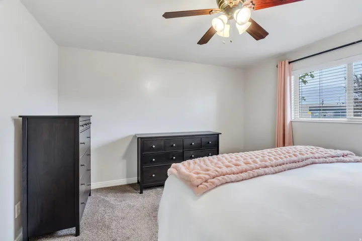 Carpeted bedroom with a ceiling fan light fixture, white walls, and a window with blinds