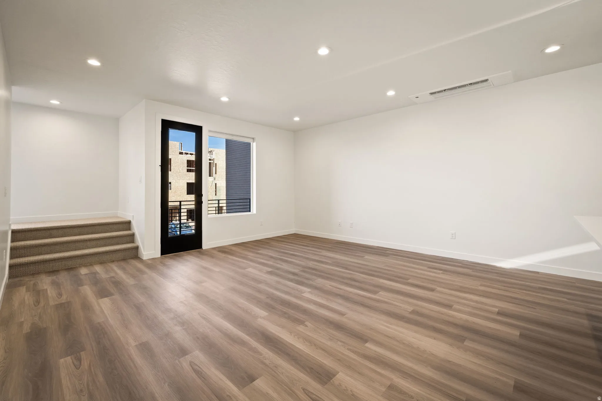 Spacious room featuring wood-finish flooring, recessed lighting, and white walls