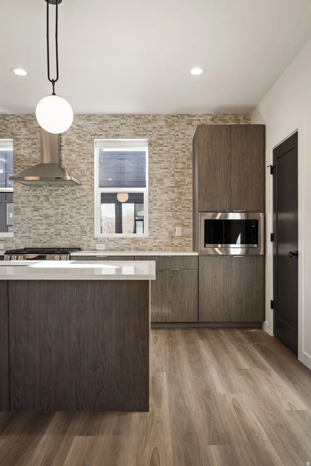 Contemporary kitchen featuring a large island with a light-toned countertop, wood-finish flooring, and cabinetry