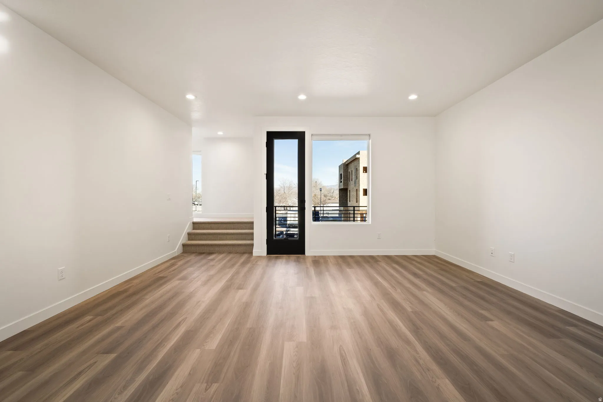 Spacious room featuring wood-finish flooring, recessed lighting, and white baseboards