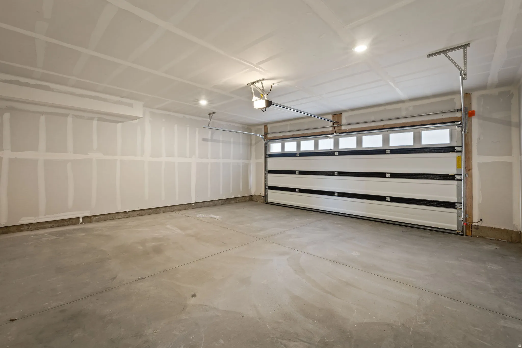 Spacious garage featuring a concrete floor, overhead lighting, and a white paneled garage door with upper window inserts