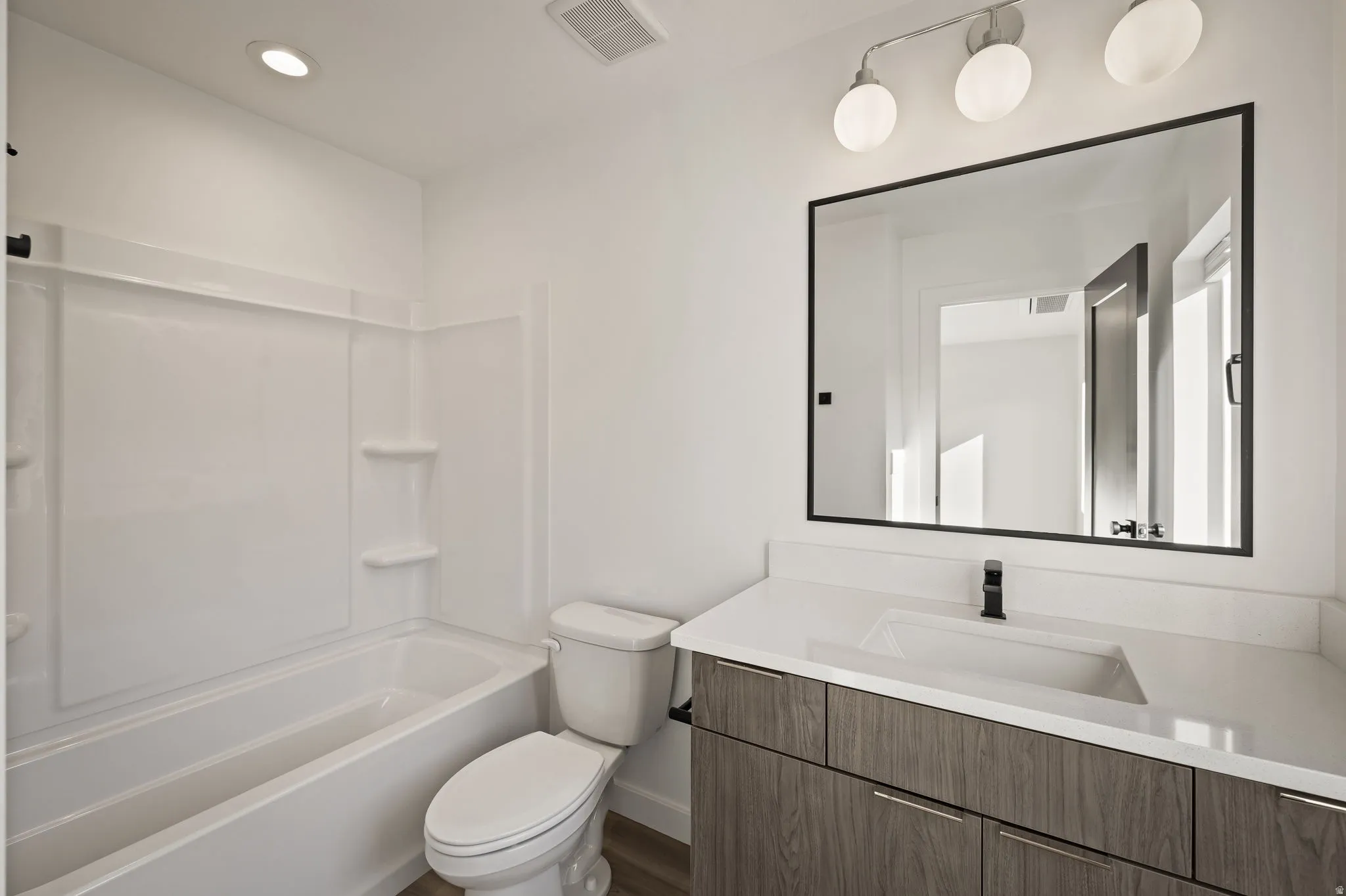 Contemporary bathroom featuring a white tub/shower combination, a wood-finish vanity with a white countertop, an integrated sink, a matte black faucet, and a large rectangular mirror with a black frame