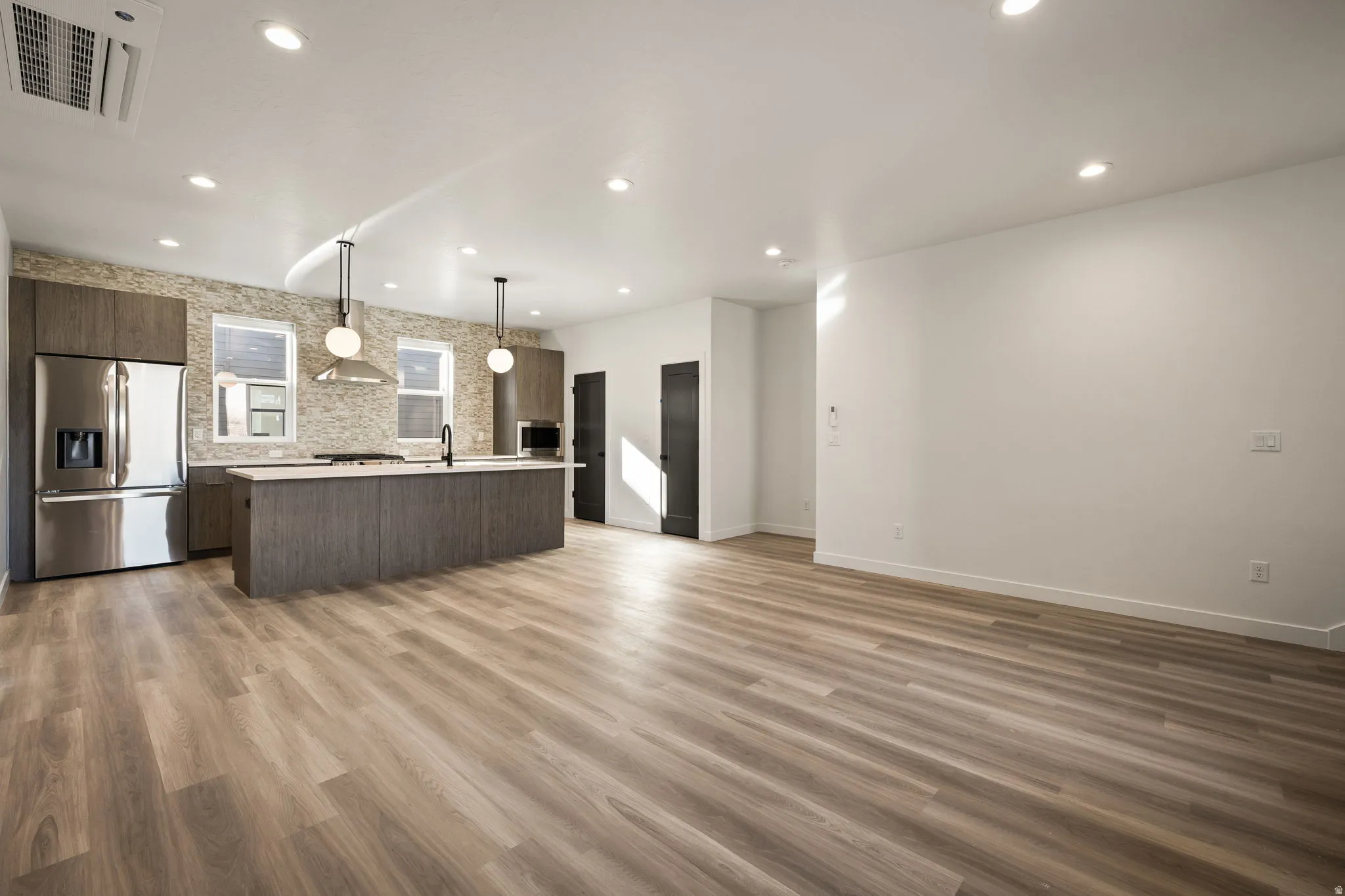 Contemporary kitchen featuring stainless steel appliances, a large island with a light-toned countertop, and modern pendant lighting