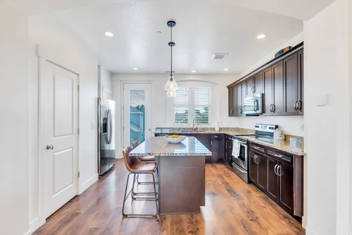 Kitchen featuring wood-finish flooring, dark wood cabinetry, granite countertops, and stainless steel appliances