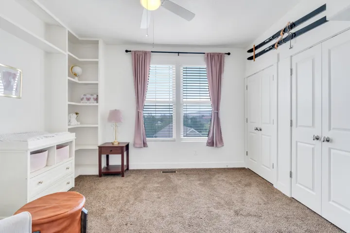 Carpeted room featuring a ceiling fan, a window with horizontal blinds, built-in shelving, and two sets of bi-fold closet doors