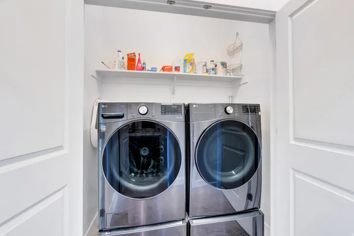 Dedicated laundry area with white panel doors, built-in shelving, and dark-finish appliances