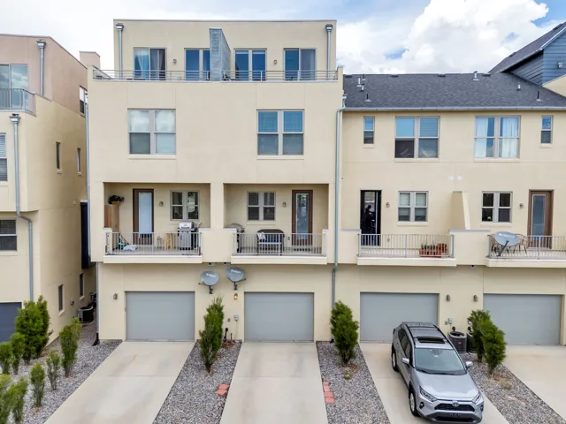 Contemporary townhome featuring a stucco exterior, multiple private balconies with metal railings, a rooftop terrace with metal railings, and a ground-level garage with a concrete driveway