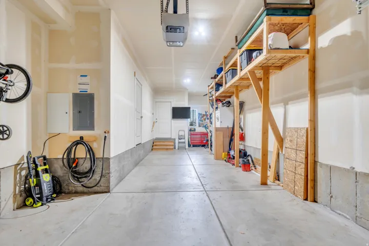 Spacious garage with exposed beam ceiling, overhead storage racks, an automatic garage door opener, and a built-in electrical panel
