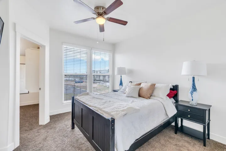 Bedroom featuring carpet flooring, crisp white walls, a ceiling fan with integrated lighting, and dual windows with horizontal blinds