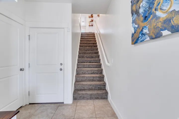 Staircase featuring carpeted treads and a white handrail, complemented by light-toned tile flooring at the base