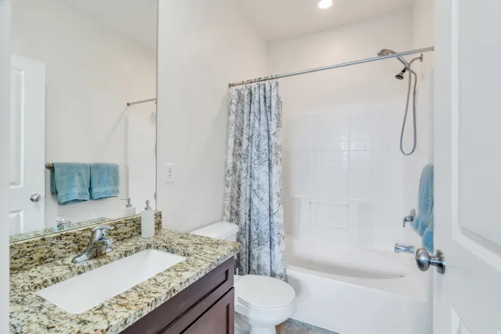 Bathroom featuring a built-in tub with a tile surround, a single vanity with a granite-finish countertop, and a large wall-mounted mirror