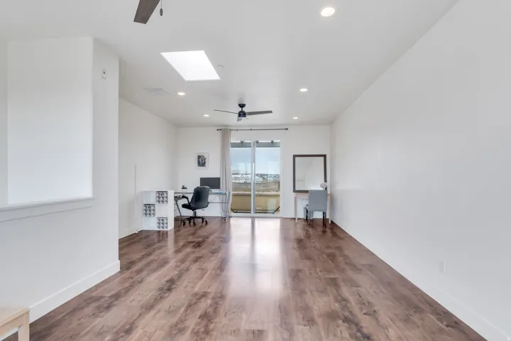 Spacious room featuring wood-finish flooring, white walls, recessed lighting, and a skylight