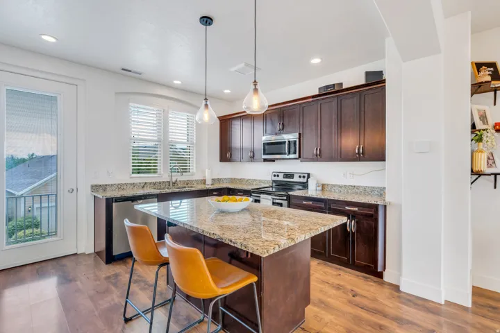 Kitchen featuring an island with stone countertop, wood-finish flooring, dark wood cabinetry with brushed nickel hardware, and stainless steel appliances