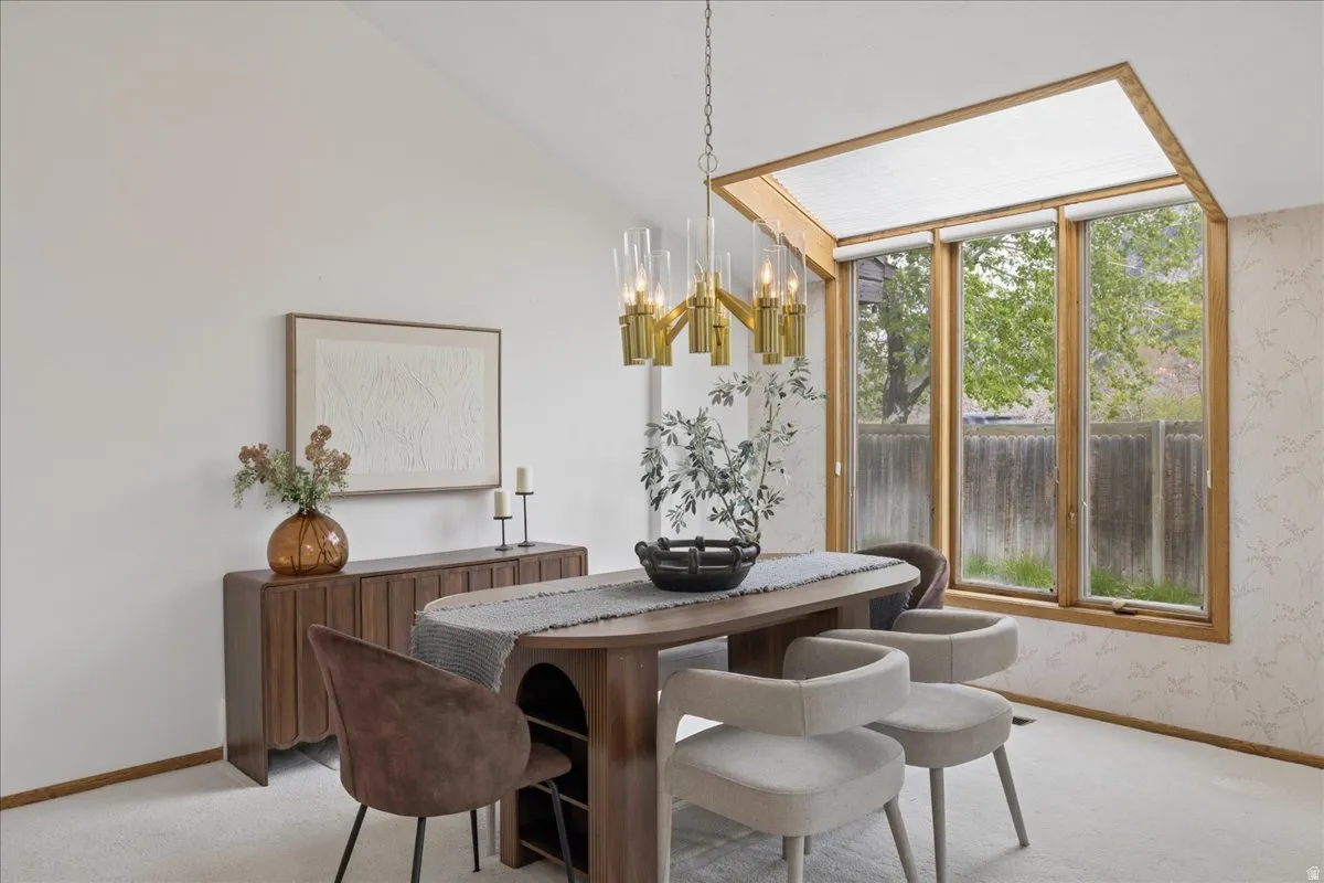 Vaulted ceiling with an angular skylight, large windows featuring wood trim, and a brass-finished chandelier with glass shades