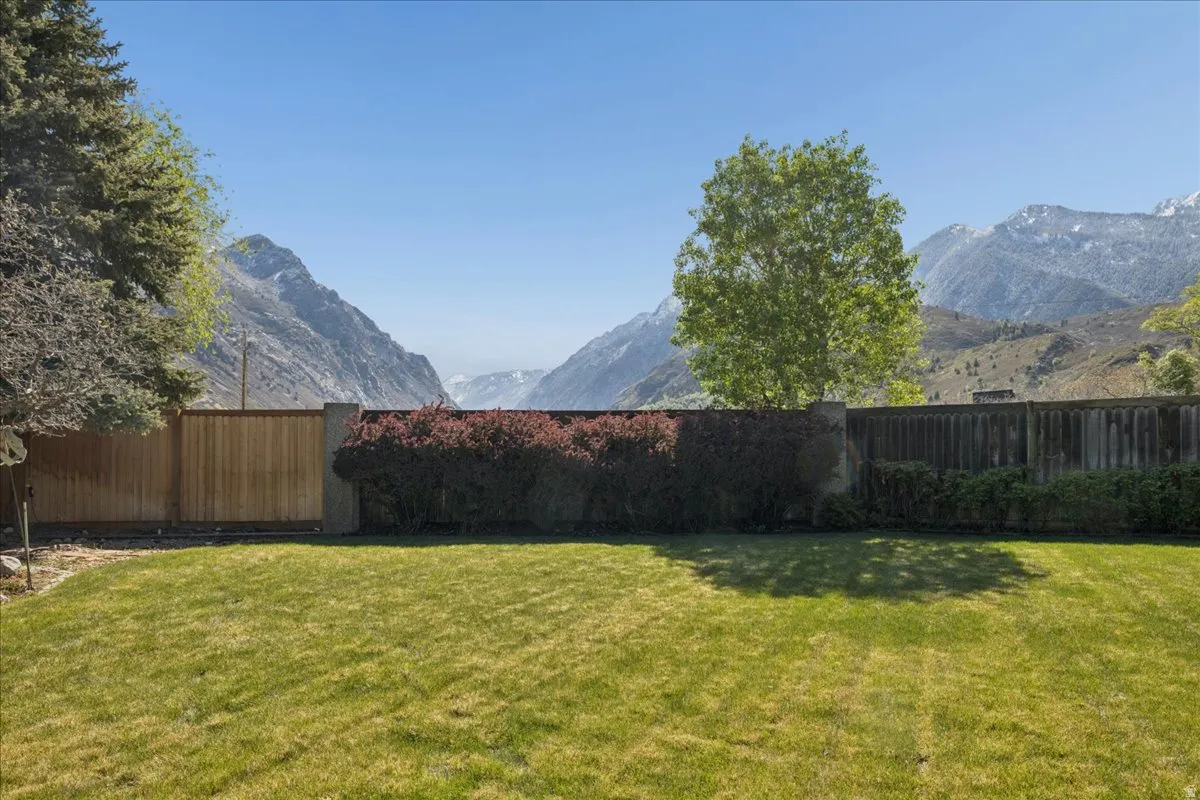 Expansive backyard featuring a manicured lawn, wood fencing, and mature trees