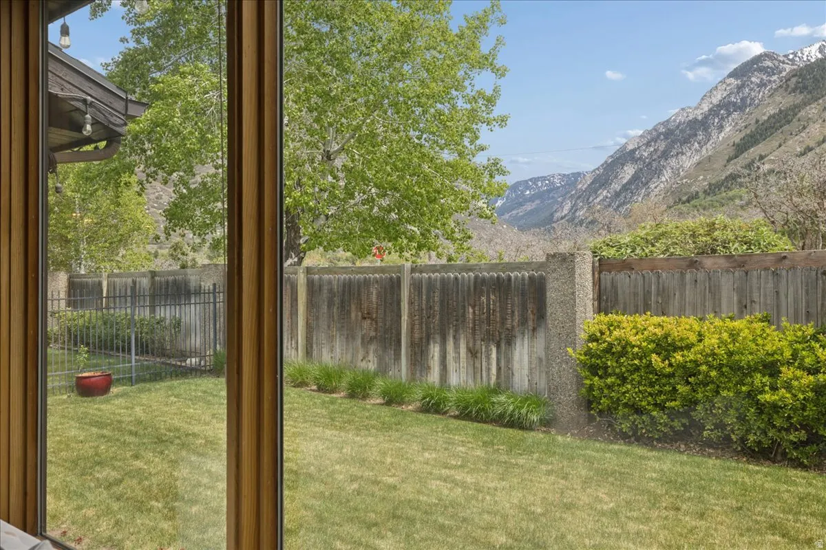 Expansive rear yard featuring green lawn, mature trees, and a combination wood and metal fence