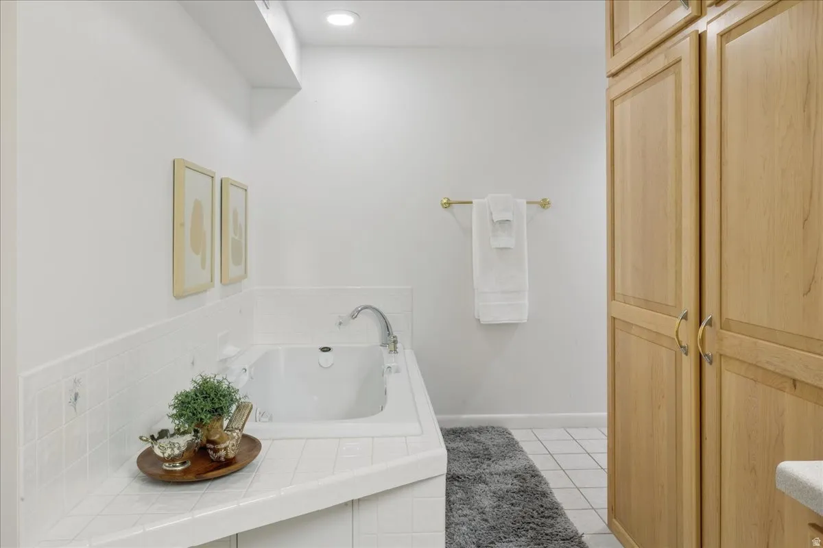 Bathroom featuring an integrated bathtub with white tile surround, a brass towel bar, and light-toned wood-finish cabinetry