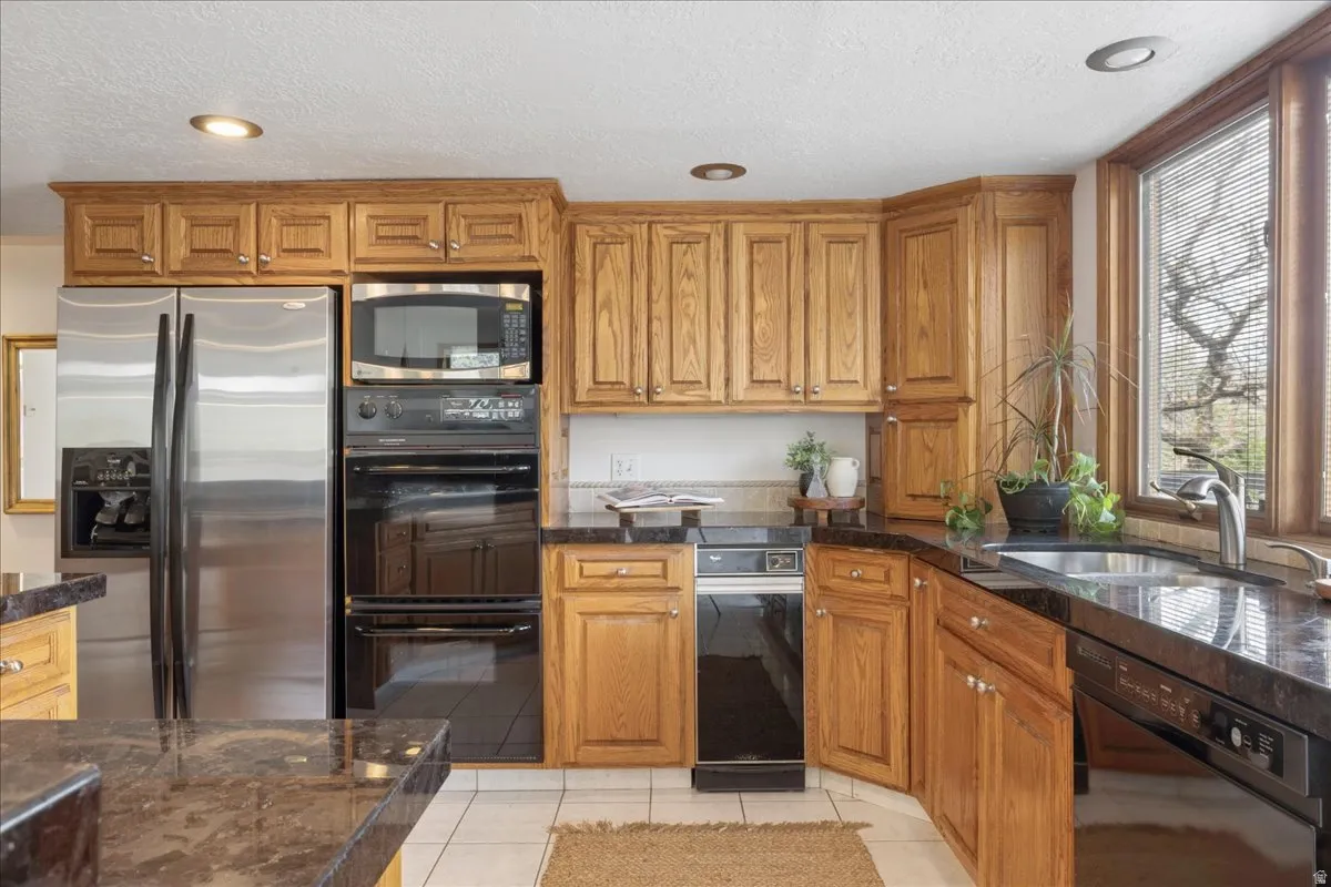 Kitchen featuring wood cabinetry, stainless steel refrigerator, built-in double oven, built-in microwave, and dark countertops