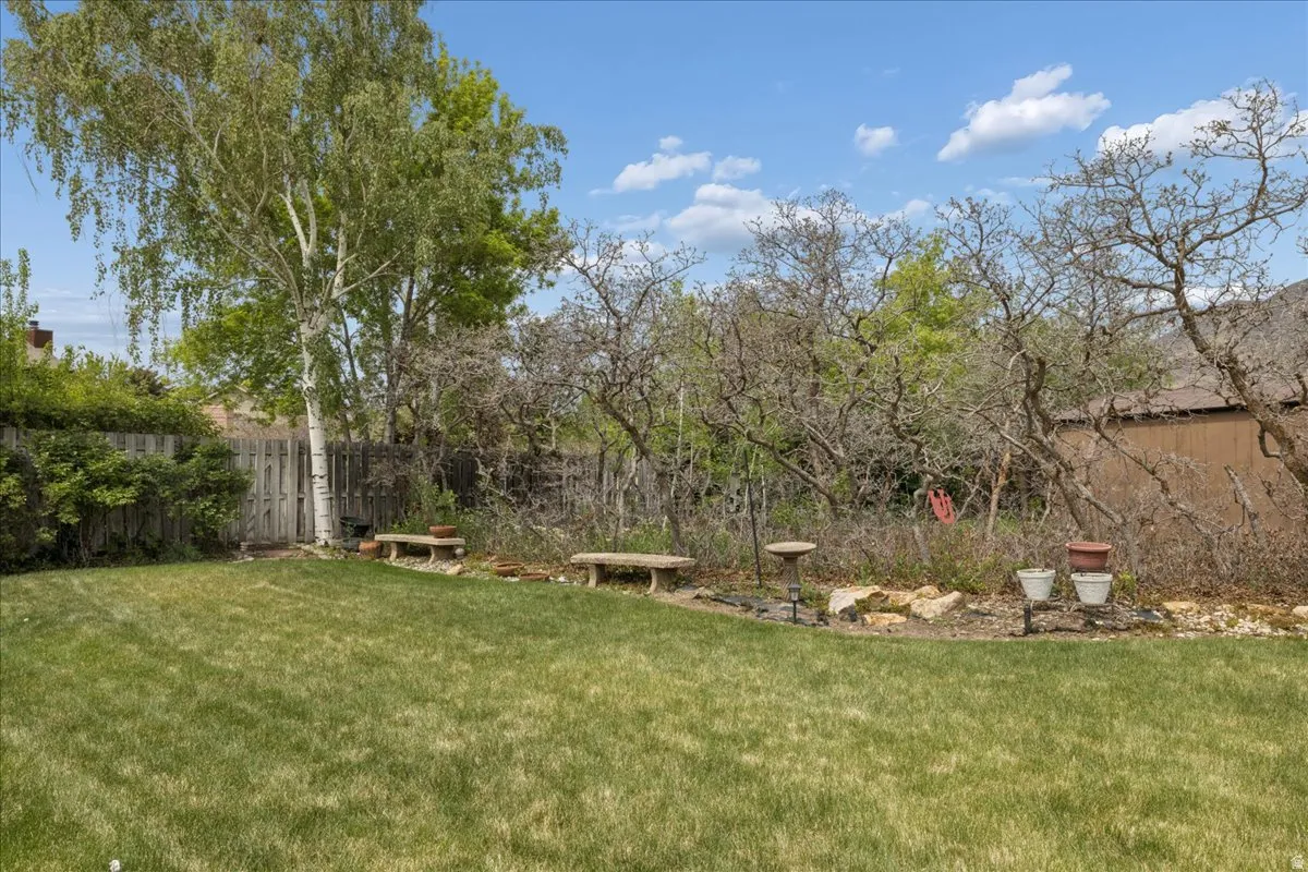 Spacious grassy yard featuring mature trees, wood fencing, and a stone-lined garden bed