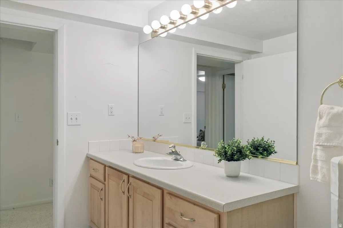 Bathroom vanity featuring light wood-finish cabinetry, a single basin sink, and a light-colored countertop