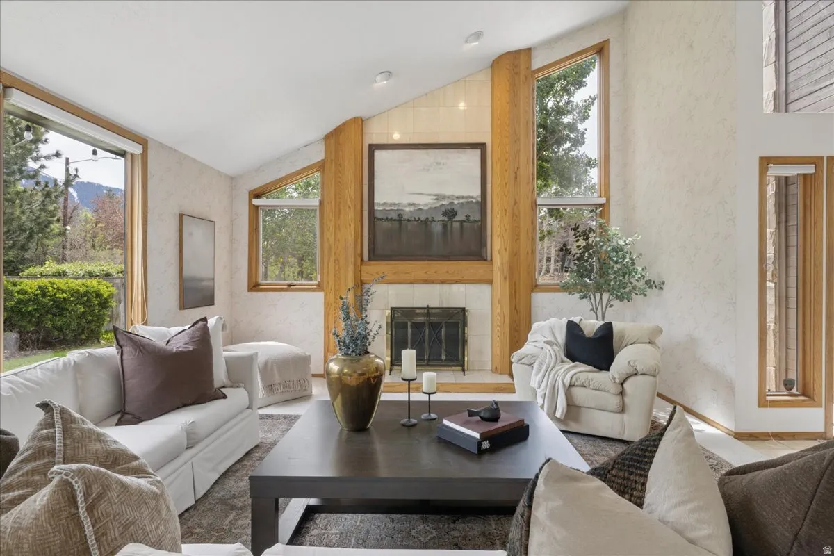 Vaulted ceiling living area featuring a fireplace with a tile surround and wood mantel, large picture windows, and wood-finish window frames