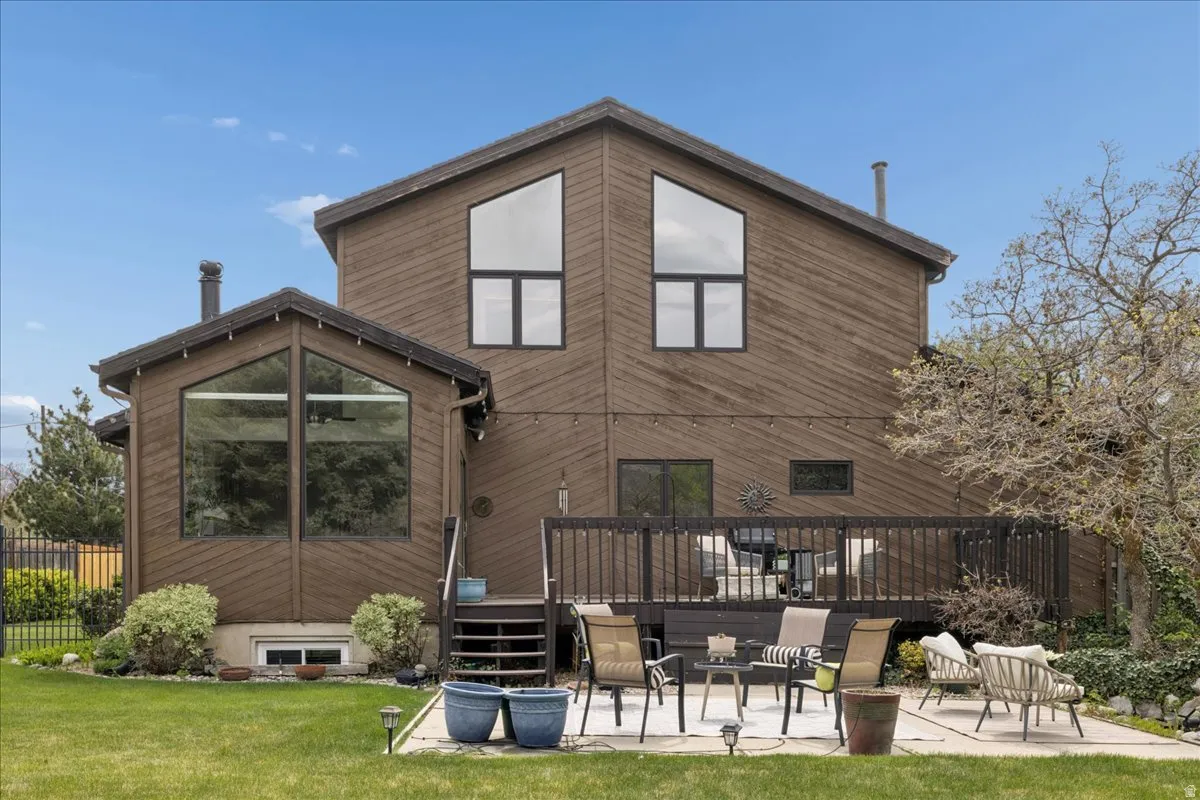 Expansive backyard featuring a manicured lawn, a concrete patio, and a raised wooden deck with railings