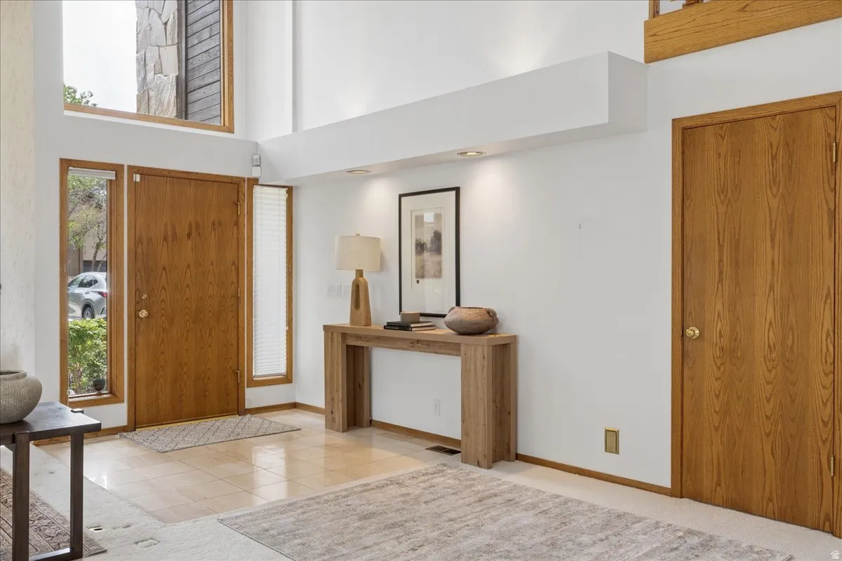 Entryway featuring a wood-panel door with sidelight windows, tile flooring, and high ceilings with upper-level windows