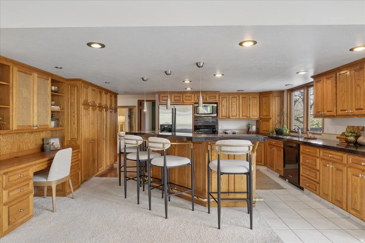 Spacious kitchen featuring extensive wood cabinetry, a large central island with seating, integrated stainless steel appliances, and recessed lighting
